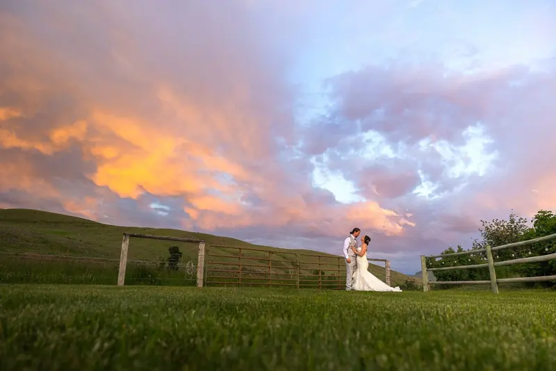 Couple by a rail fence under a pink and gold sunset